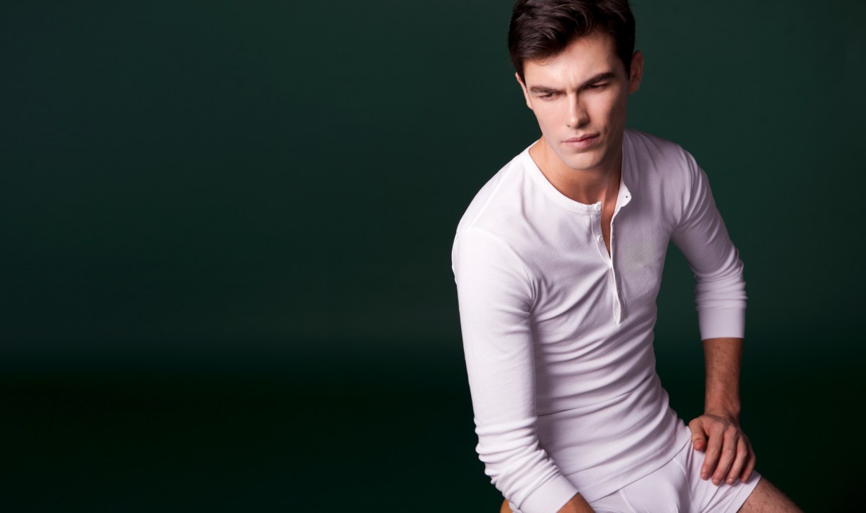 Man wearing a white long-sleeved henley shirt against a green background.