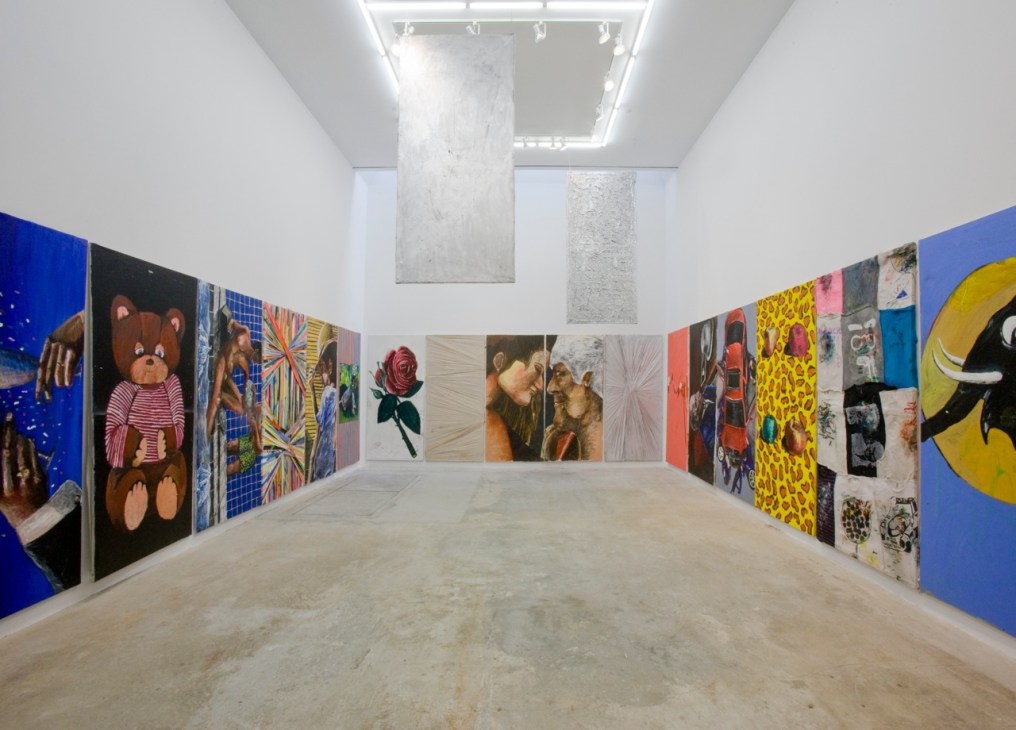 Interior of a contemporary art gallery with colorful paintings and mixed media works displayed on white walls.