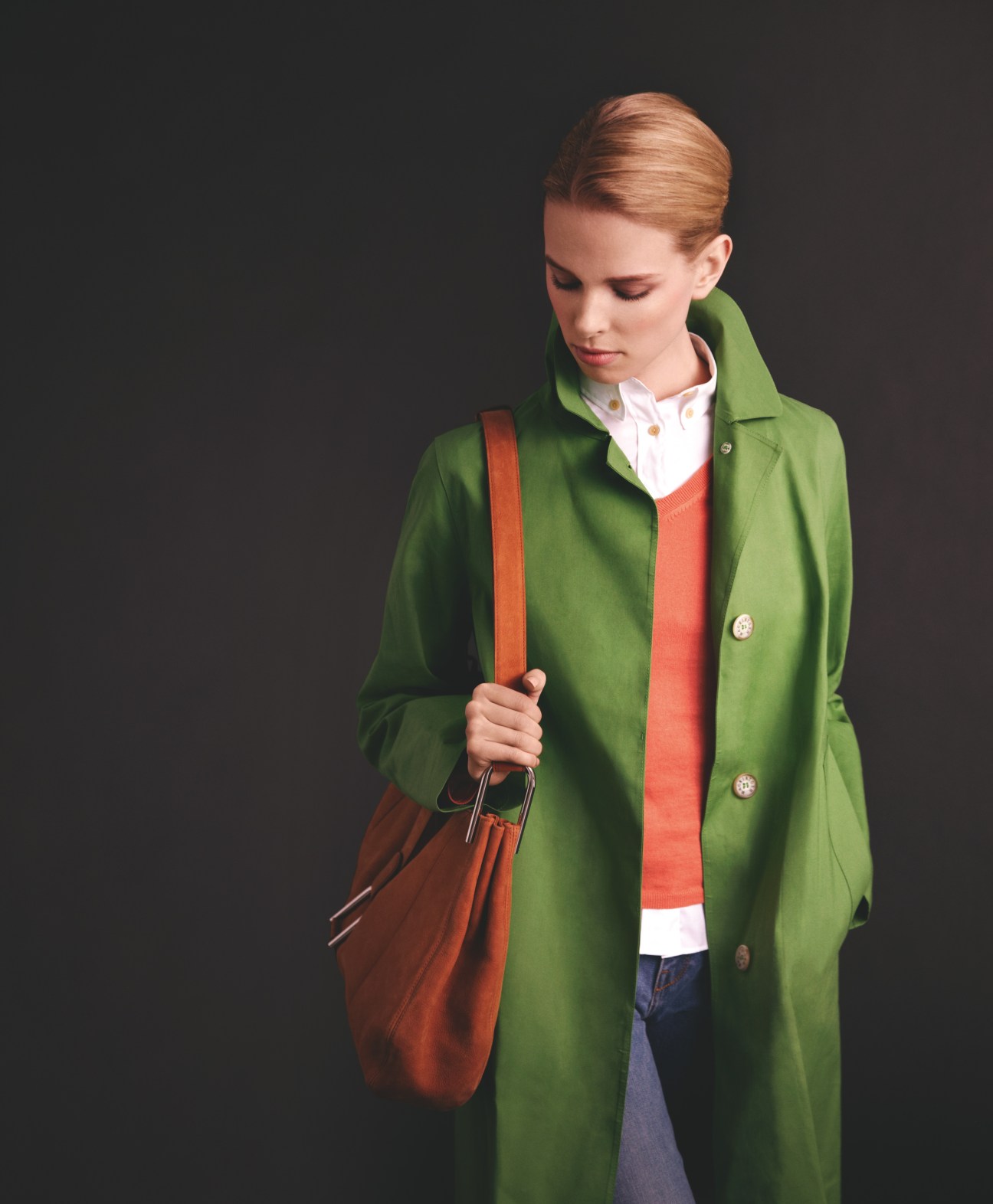 Model wearing a bright green Mackintosh coat over a red v-neck jumper and white shirt, carrying a rust-colored Delvaux bag.
