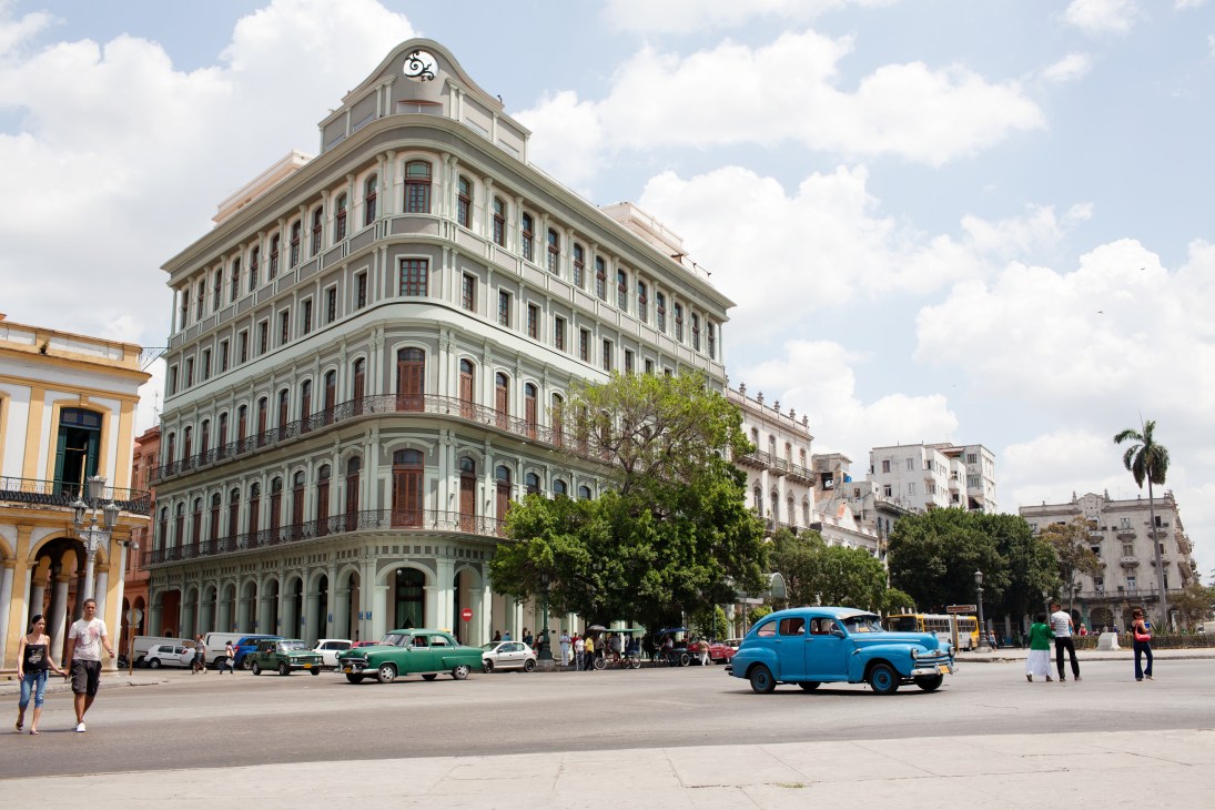 Historic colonial building with classic cars parked in front on a Havana street.