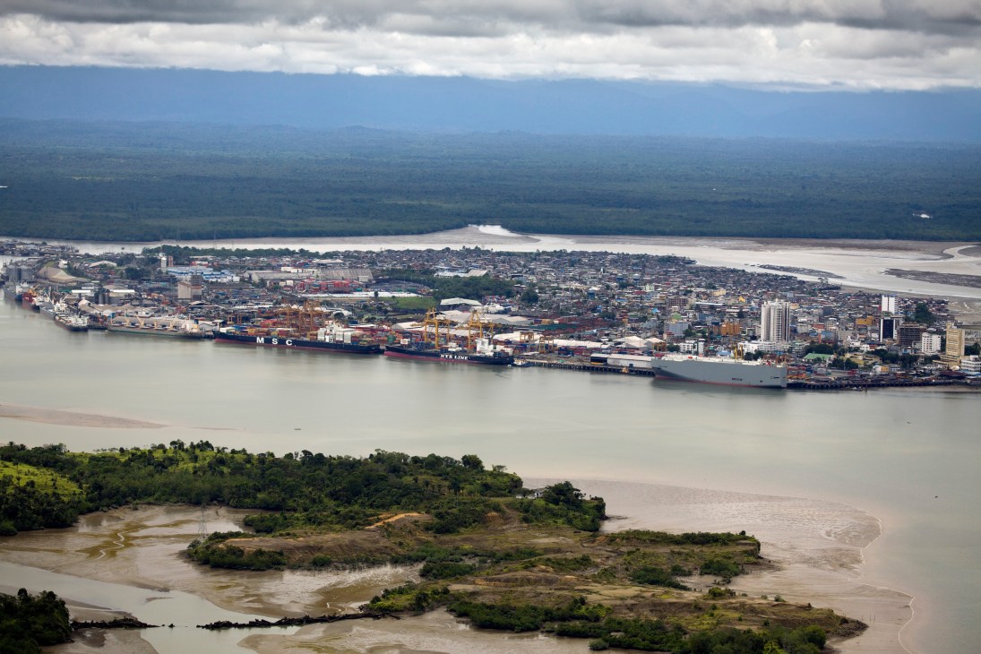 Aerial view of Buenaventura port with cargo ships, container cranes, and the city surrounded by muddy rivers and rainforest.