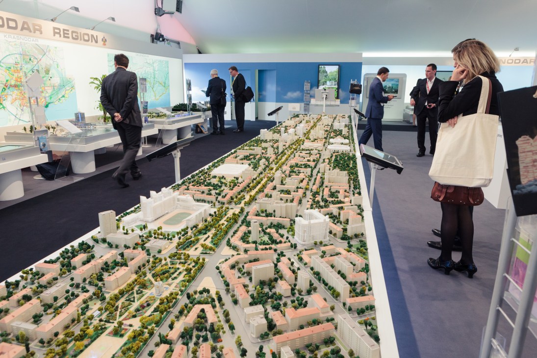 Architectural scale model of Krasnodar urban development displayed at Russian Federation booth with visitors and signage.