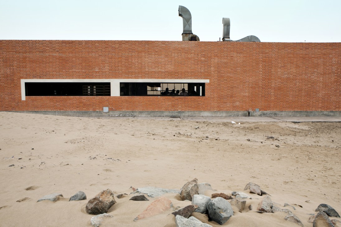 Modern red-brick single-storey cooking school building with white-framed windows on sandy desert terrain.
