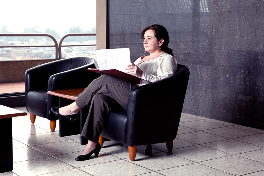 Claudia Paz y Paz, Guatemala's attorney general, sits in a black leather chair holding documents with a city view behind her.