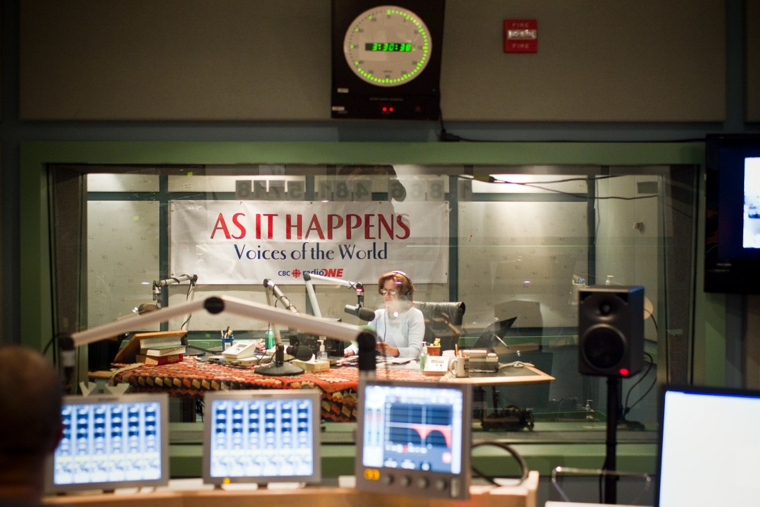 A woman broadcaster seated at a desk in a CBC Radio studio, with microphones and equipment visible.