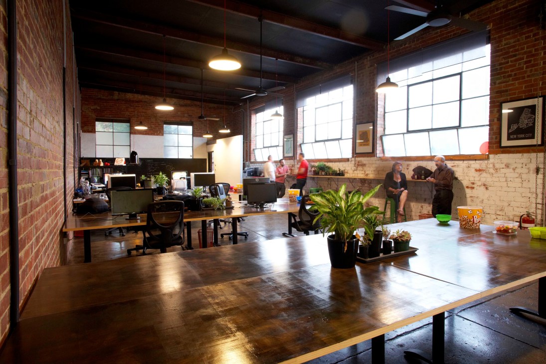 Interior of The House of Commons design studio in Melbourne featuring red brick walls, polished concrete floors, and industrial warehouse architecture with workers and natural light.
