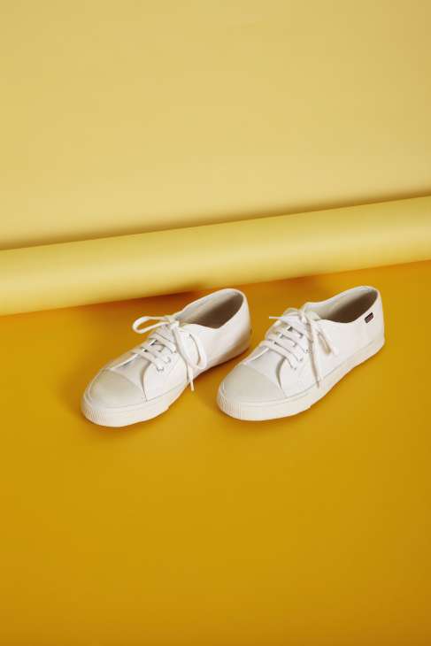 Pair of white canvas sneakers with cream rubber sole on yellow background.