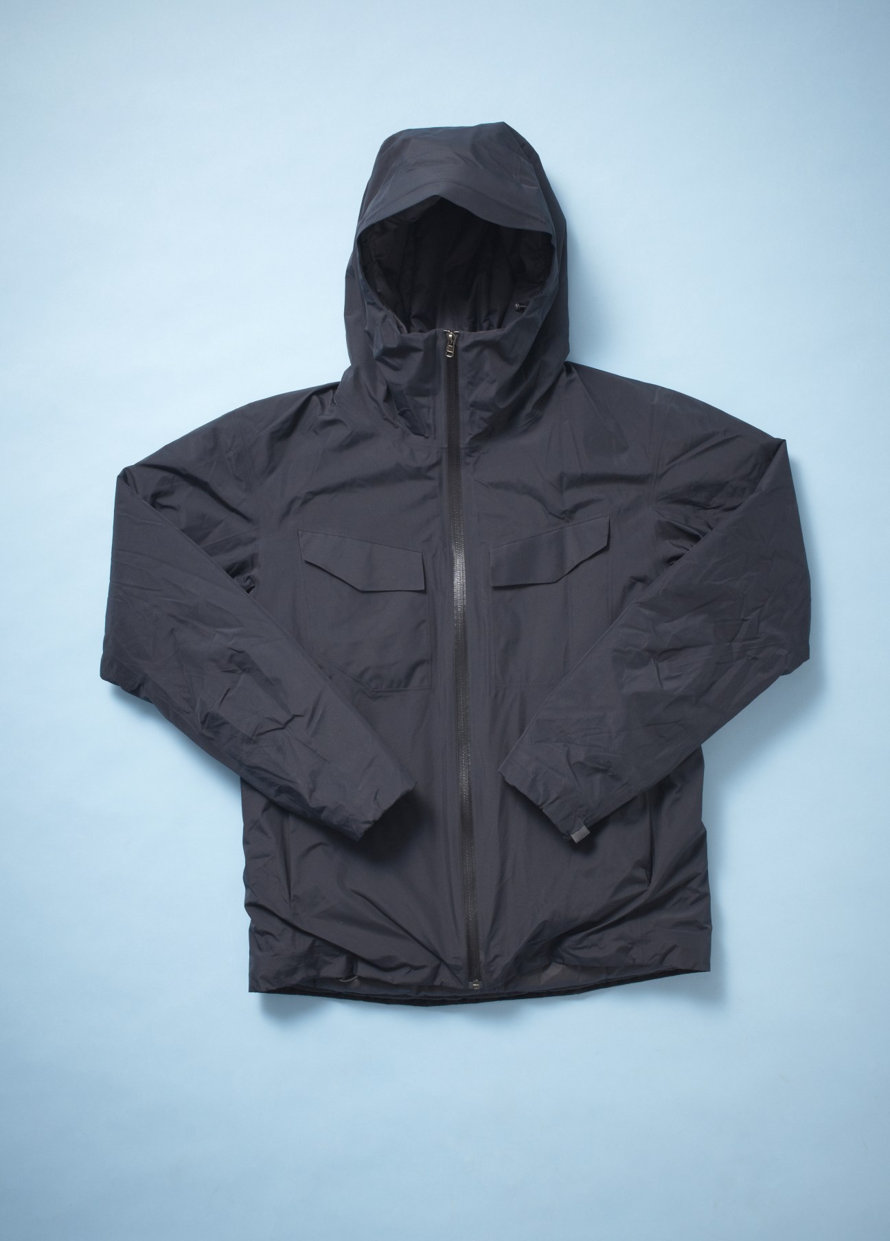 Black Arc'teryx Veilance packable jacket with hood laid flat against light blue background.