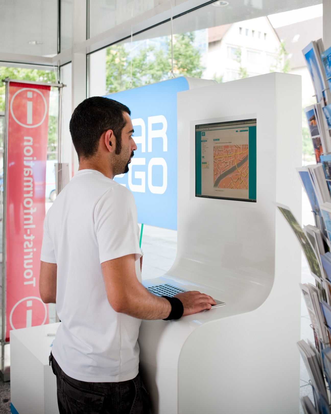 Man using a Car2Go booking kiosk with map display in a customer centre.
