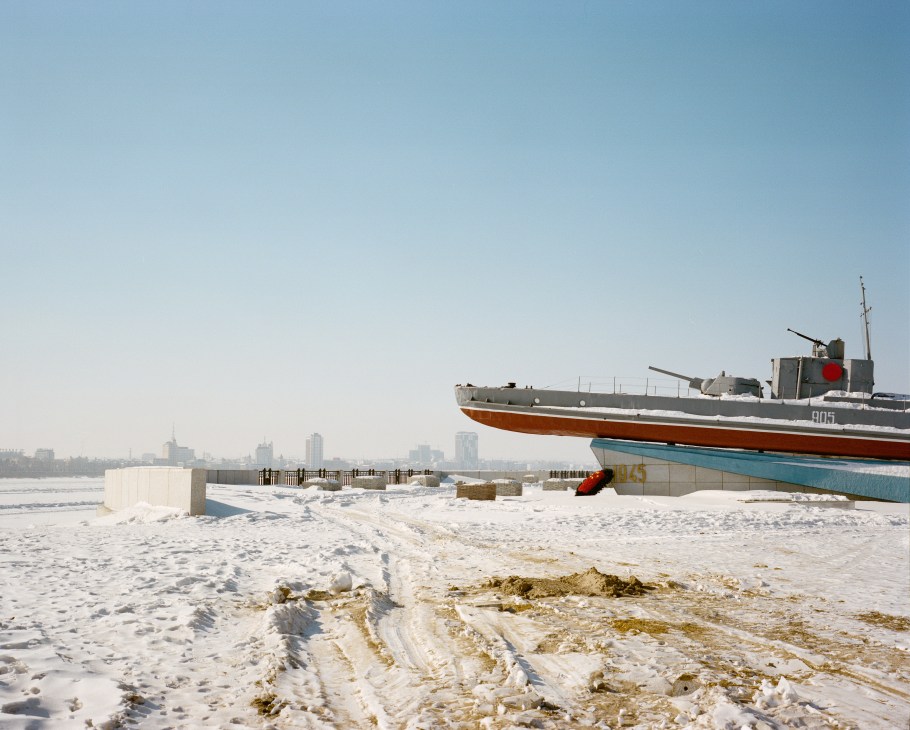 Russian gunboat war memorial with cannons on the frozen Amur River bank in Blagoveshchensk, with Chinese city skyline visible across the ice.