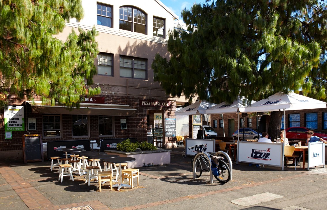 Pizza Piatsa courtyard with outdoor seating, white umbrellas, and bicycles on a sunny day