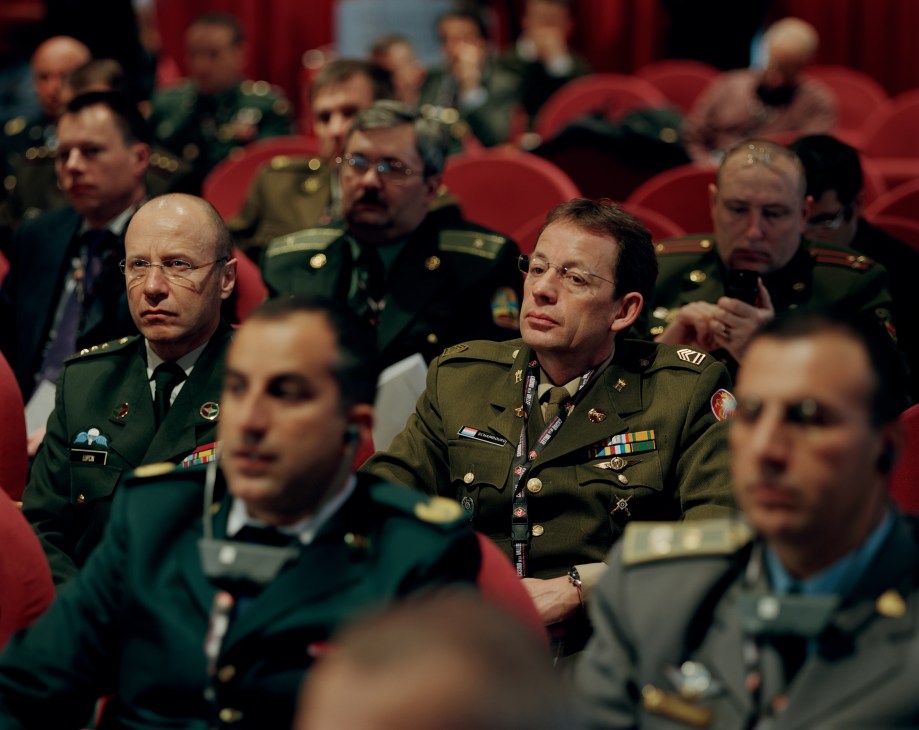 Military officers in uniform seated in red chairs at an indoor forum discussion.