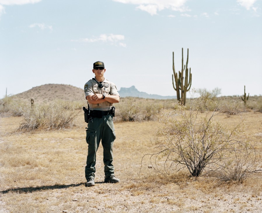 Deputy Sheriff Ashton Shewey stands in desert landscape wearing uniform and sunglasses.