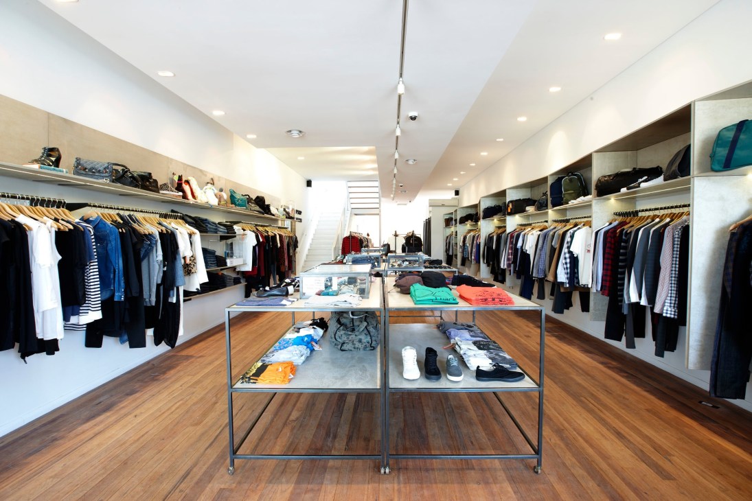 Interior of Incu boutique with wooden floor, display tables, and clothing racks lining white walls.