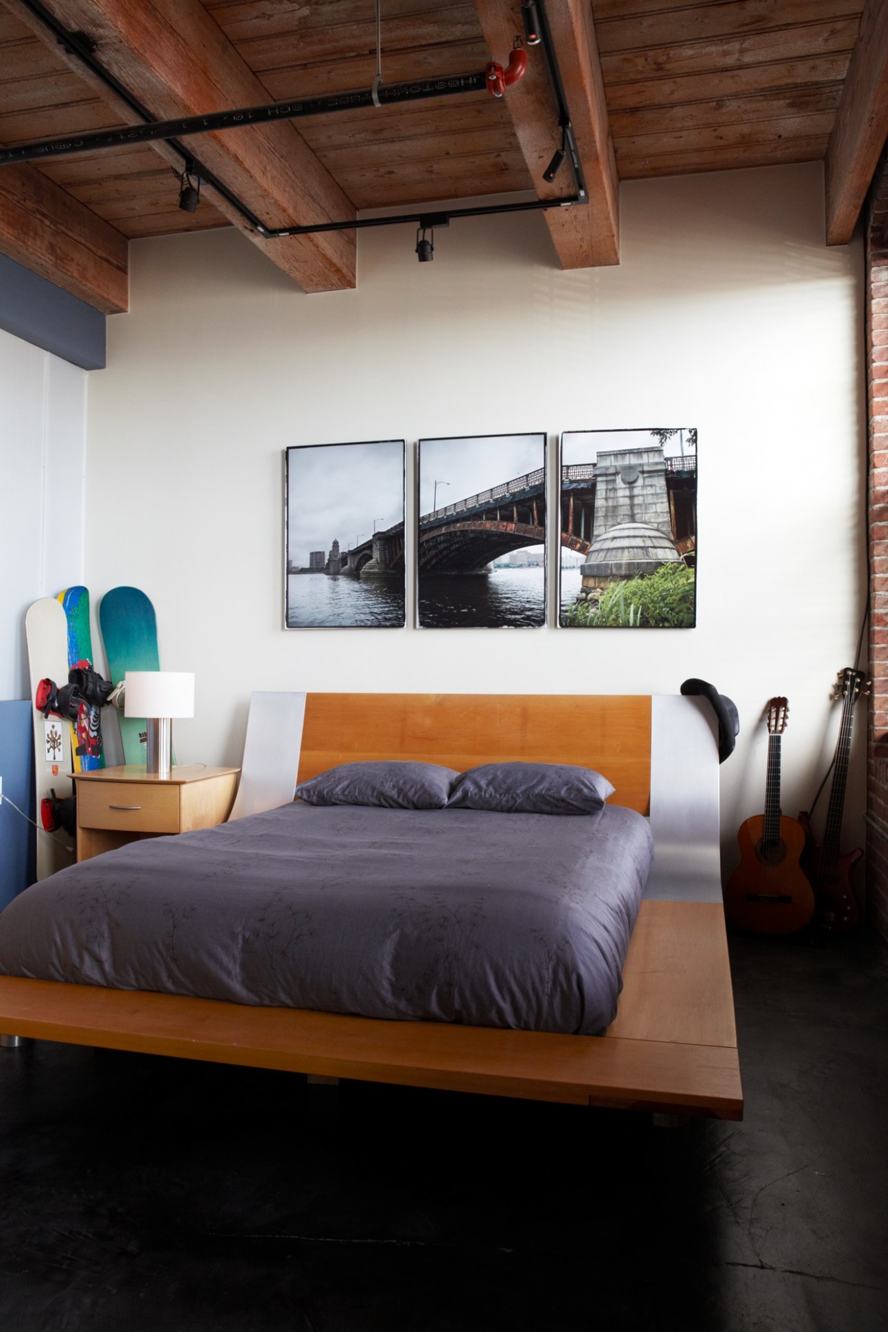 Modern bedroom with wooden beams, orange headboard, and bridge photographs on white walls.