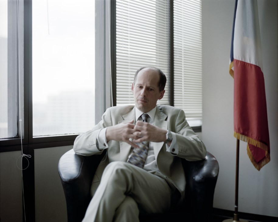 Consul-general Olivier Brochenin seated in an office chair with a French flag visible in the background.
