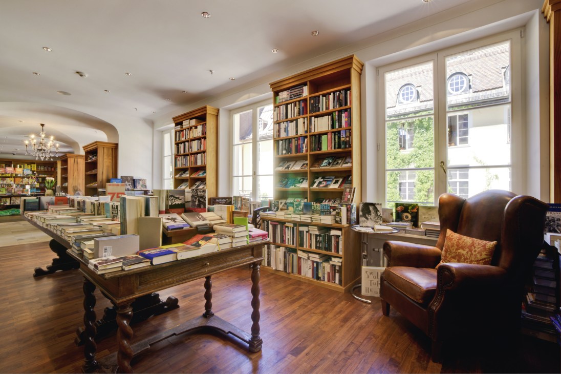 Library interior at Schloss Elmau with wooden bookshelves, leather wingback chair and reading tables.