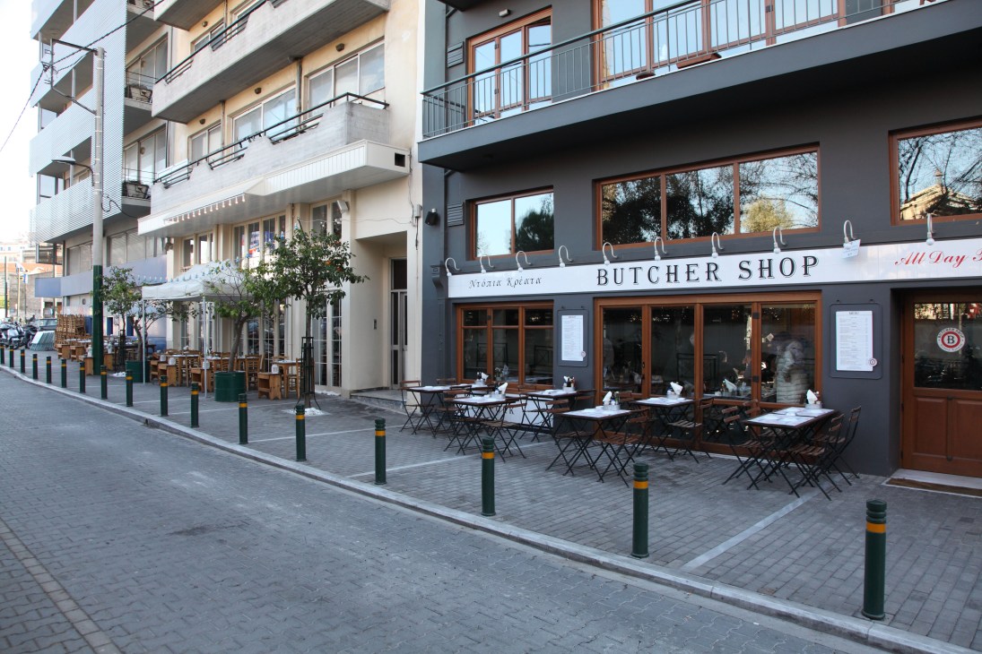 A butcher shop with outdoor seating on a quiet Athens street lined with modern apartment buildings.