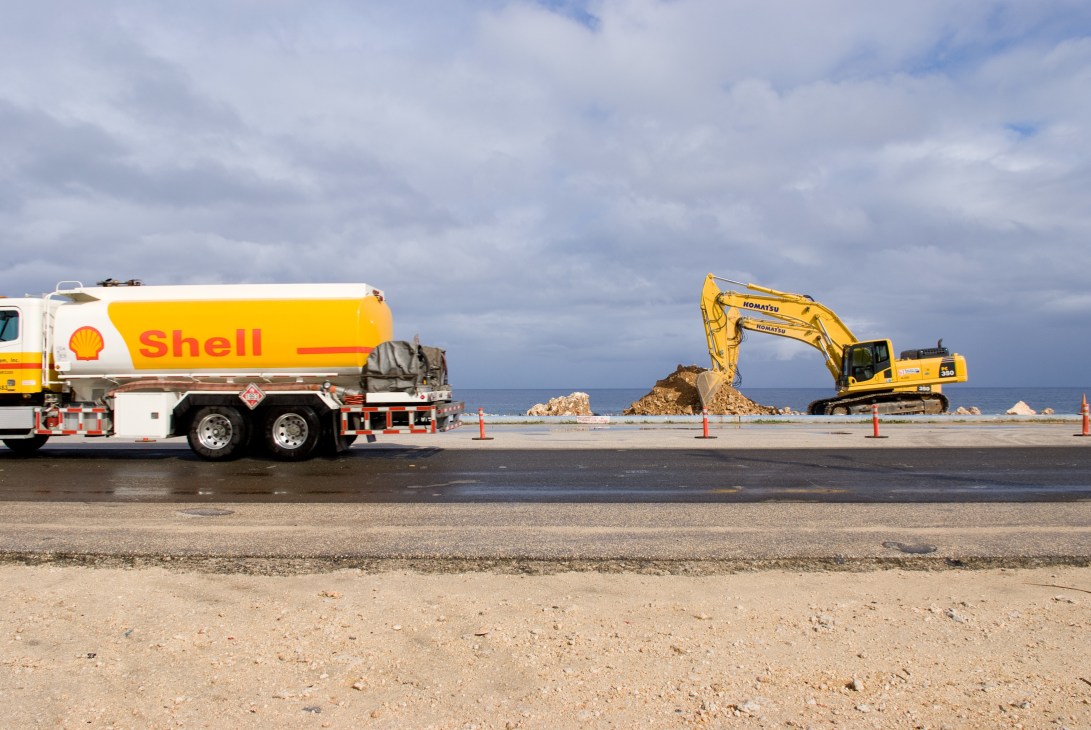 Shell tanker truck and yellow Komatsu excavator on a beach construction site in Guam.