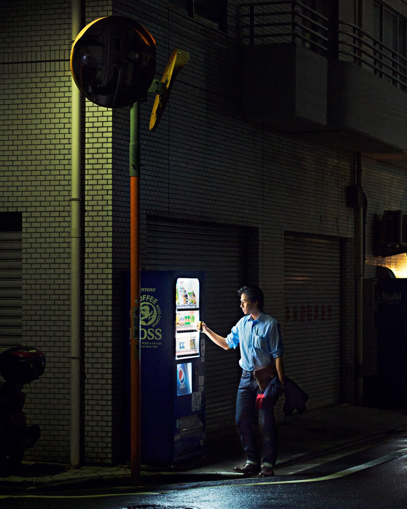 Man in blue shirt and dark trousers using a vending machine at night on a Tokyo street.