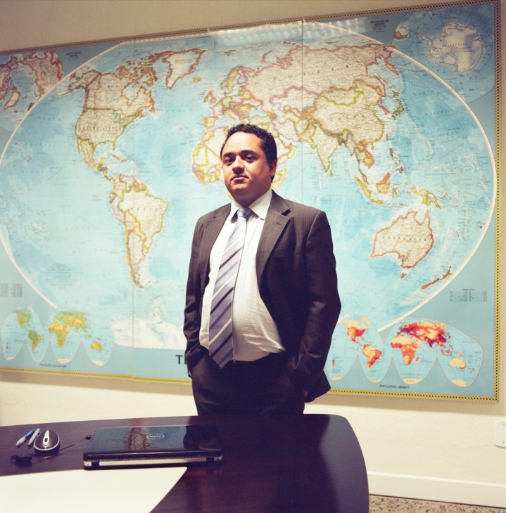 Man in business suit standing at desk in front of large world map display.