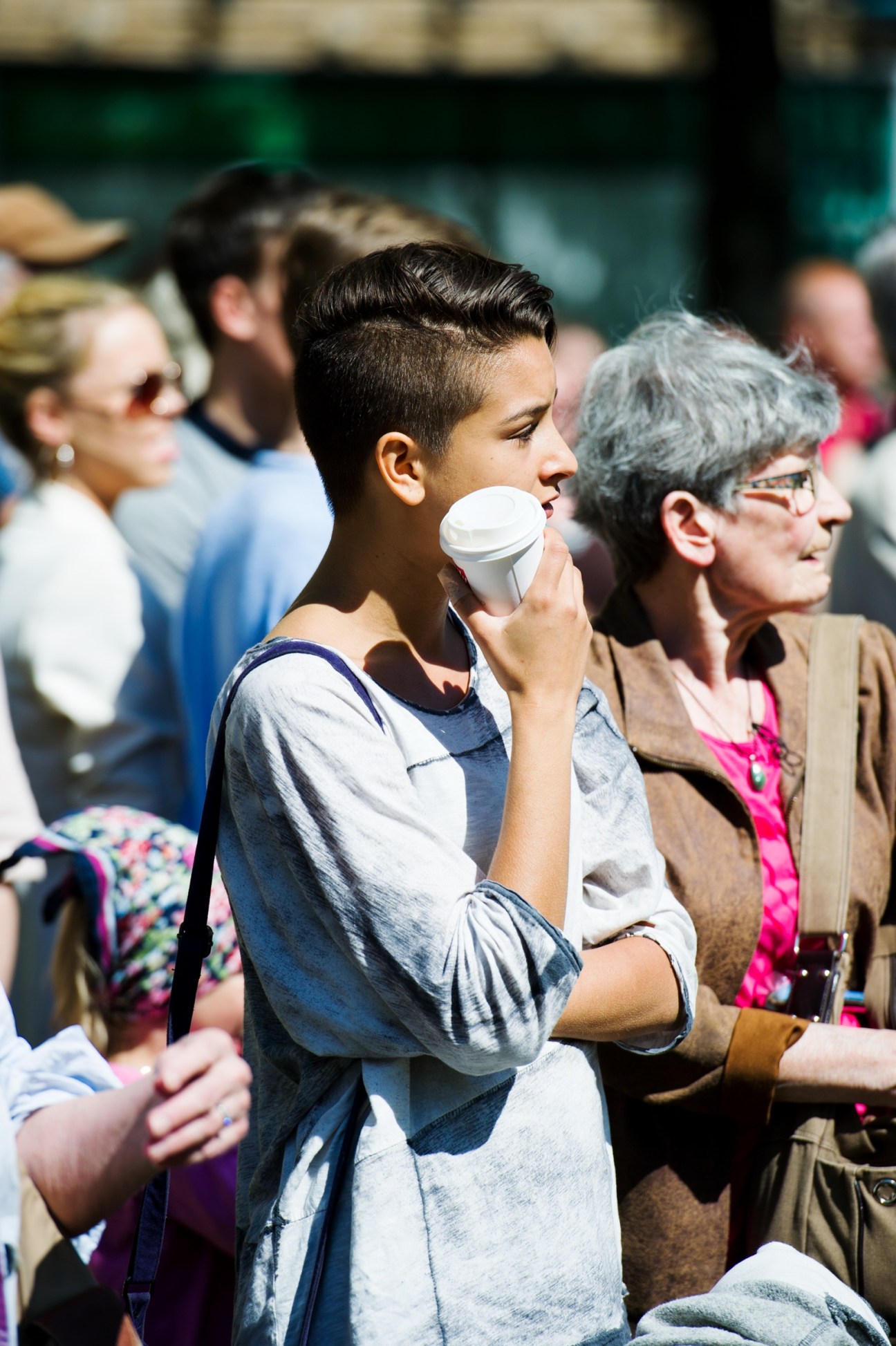 Young boy eating ice cream outdoors among a crowd of people on a sunny day.