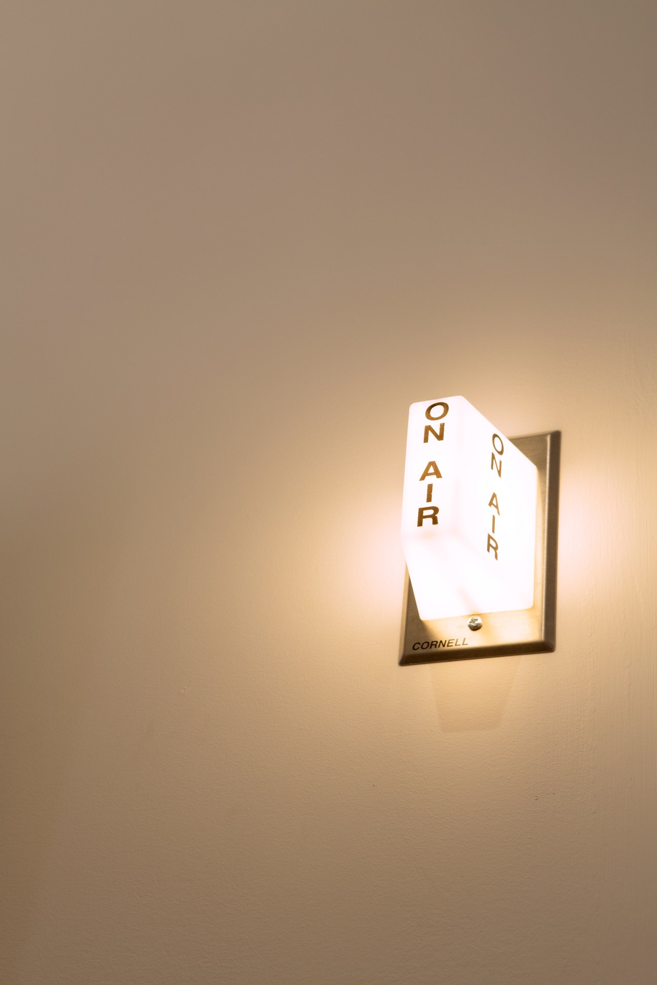 A white illuminated sign reading 'ON AIR' mounted on a beige wall in a brass frame.