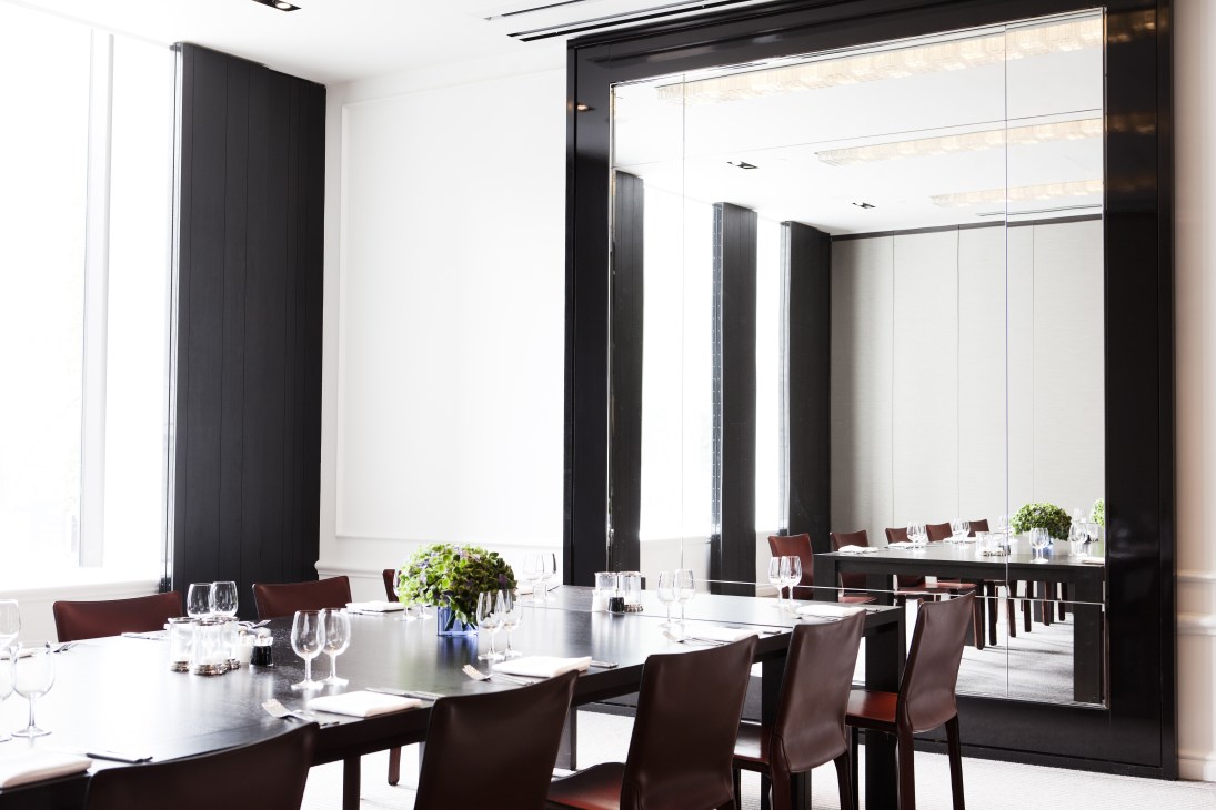 Modern dining room with long black table, burgundy chairs, floor-to-ceiling mirror, and black structural columns.