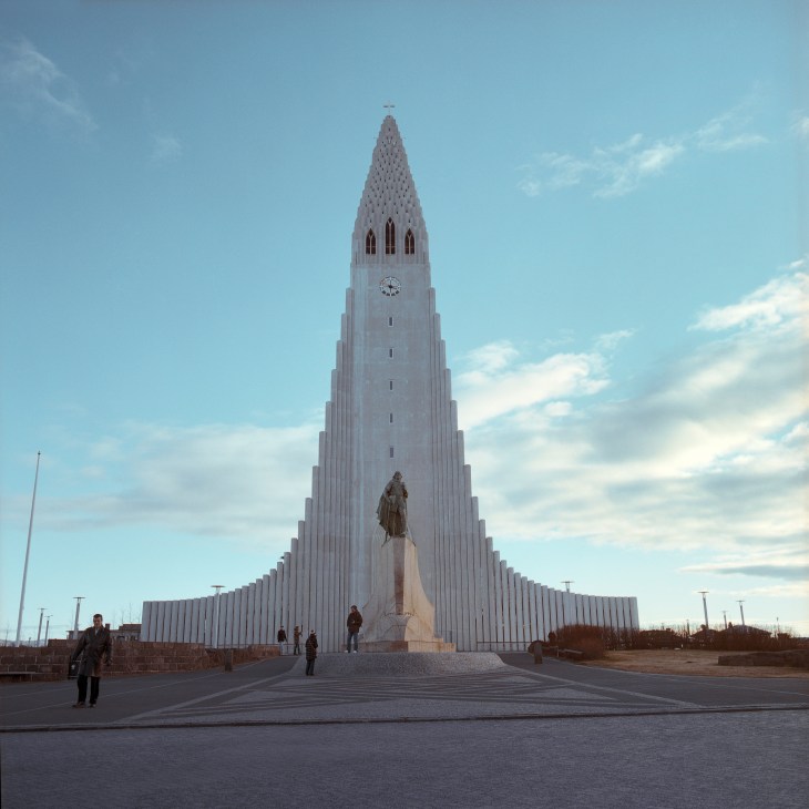 Hallgrimur church's white concrete spire towers against a blue sky with a statue in front.