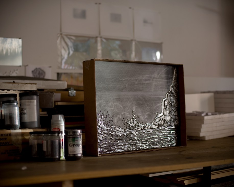 Graphite relief artwork titled 'Nocturnal (Cinematic Pour)' displayed in artist's studio with landscape details visible in polished surface.