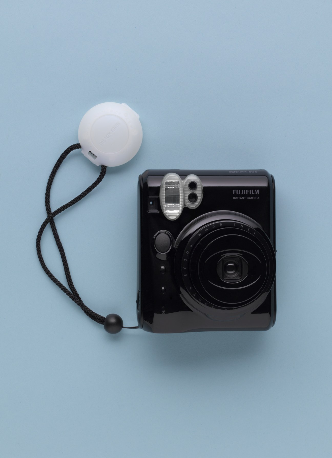 Fujifilm Instax mini50S Cheki instant camera in black with white flash and black wrist strap on blue background.