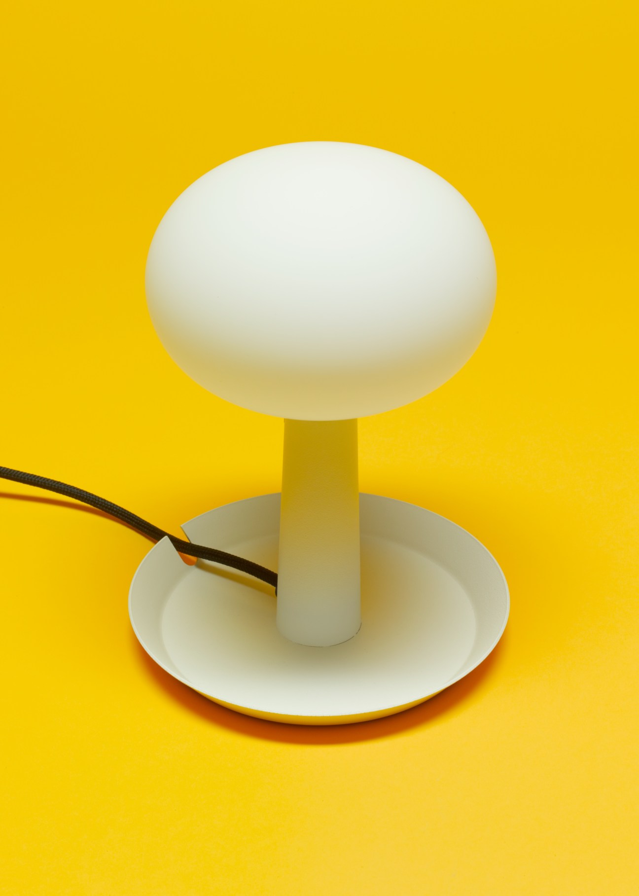 White opal glass globe lamp on circular tray base with black cord against yellow background.