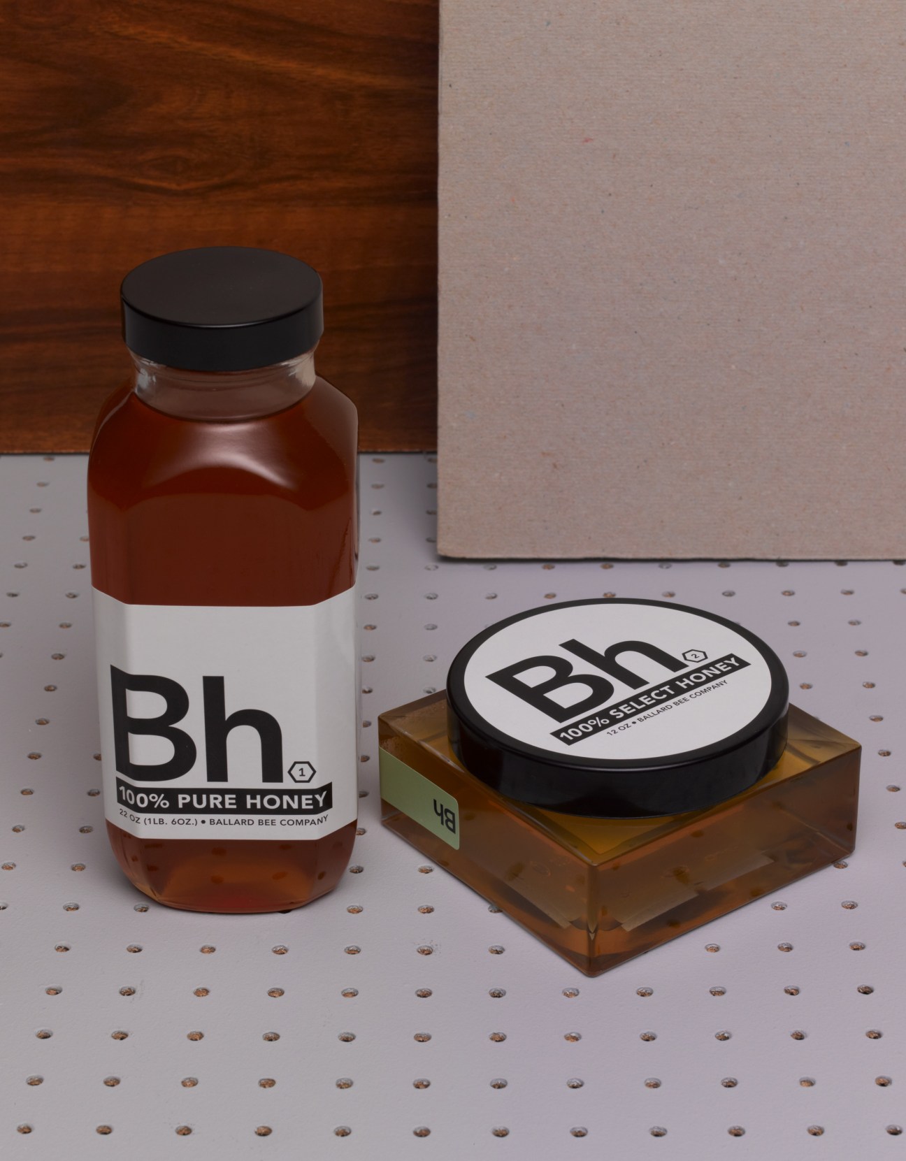 Ballard Bee Company raw honey in a glass jar with black cap and wooden honey pot with black lid.