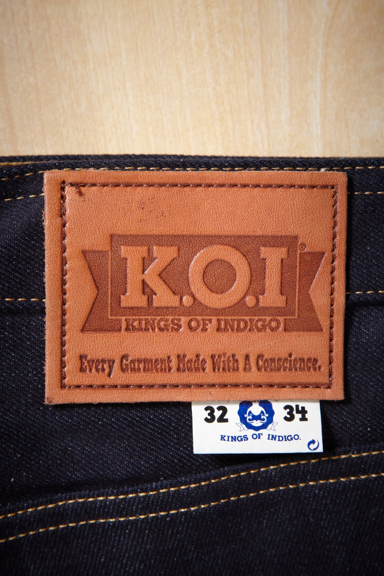 Close-up of Kings of Indigo (KOI) leather jeans label on dark denim with size tag.