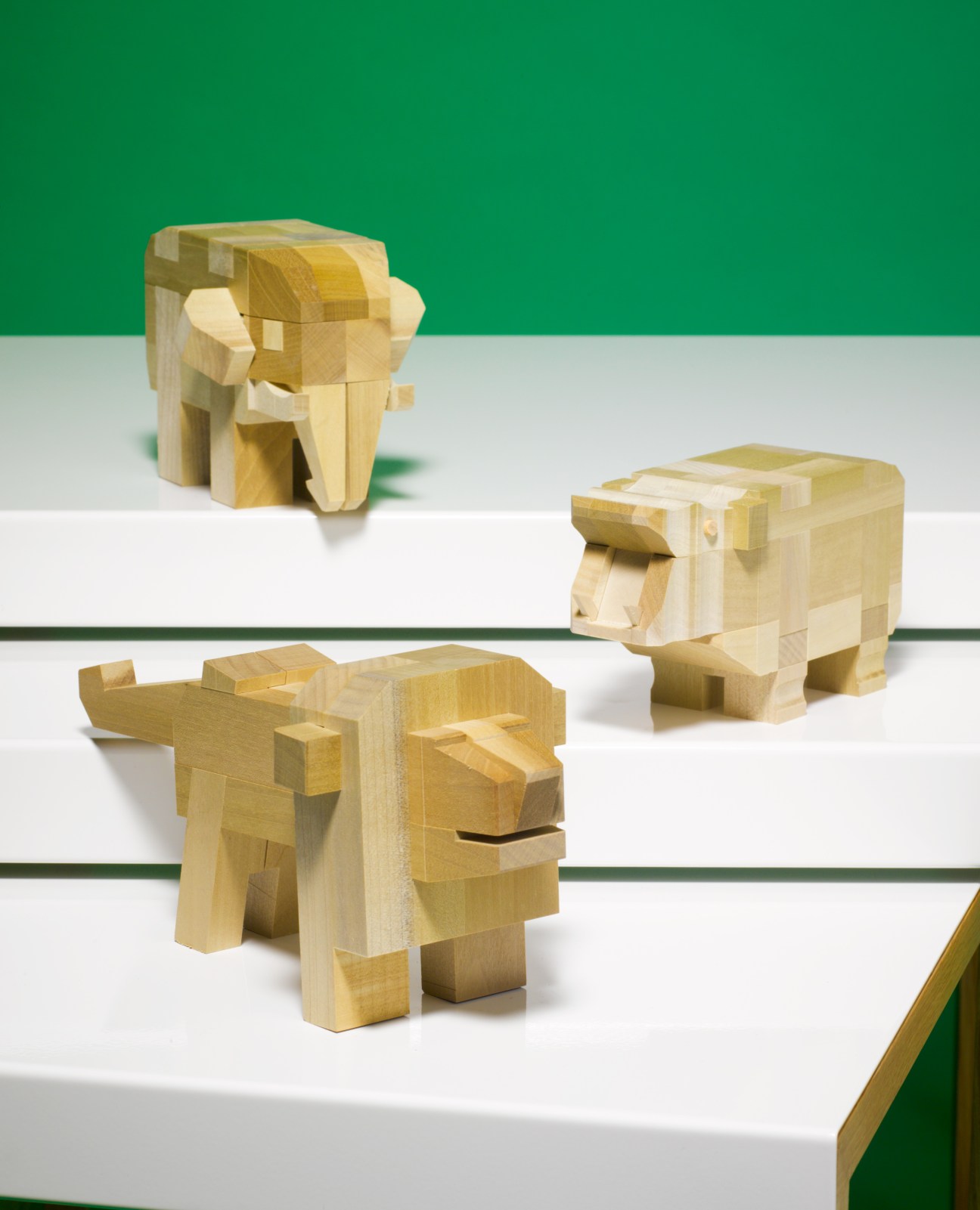 Three wooden animal puzzle toys with interlocking geometric blocks on white shelves against a green wall.