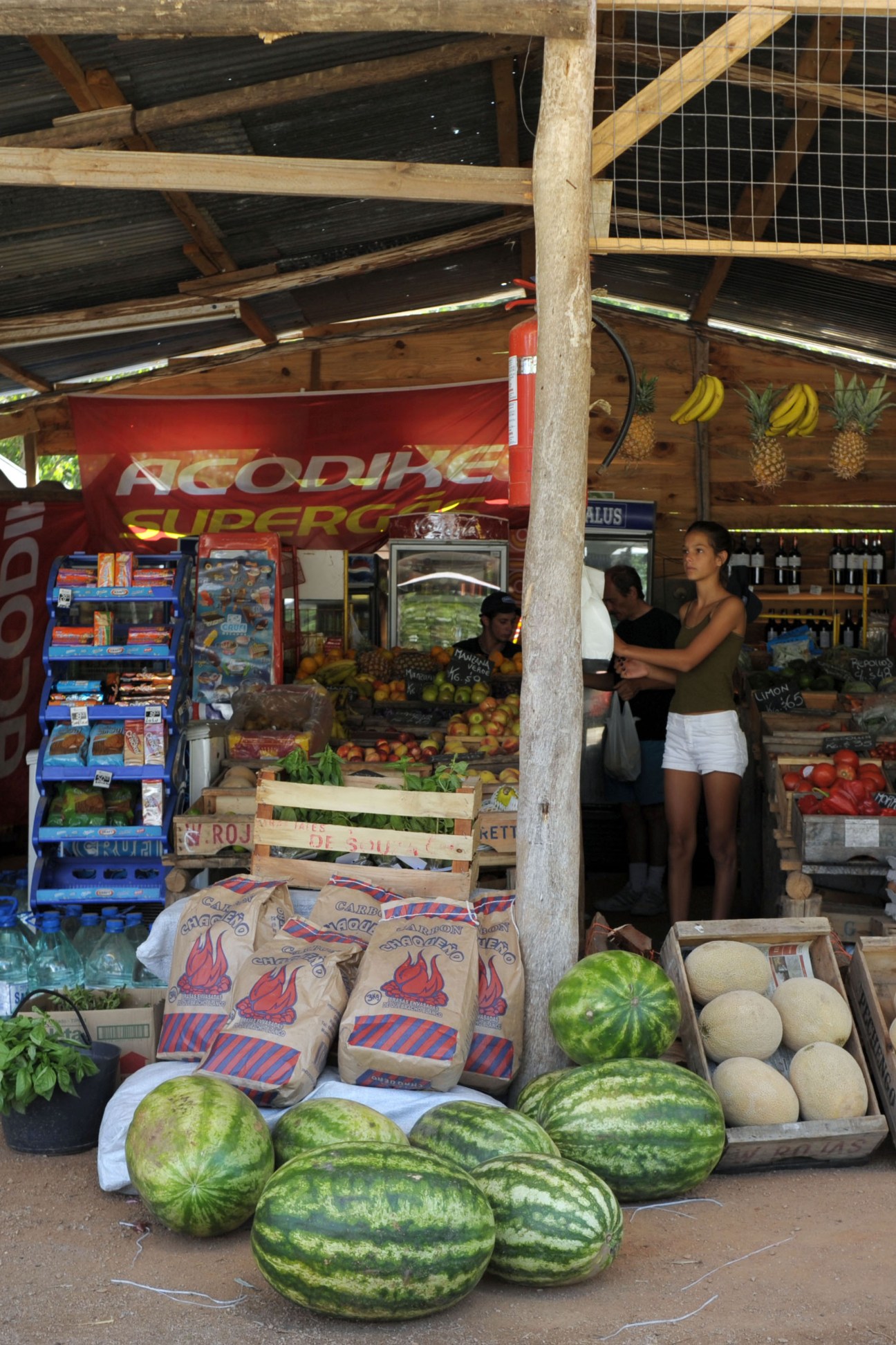 El Tomate Alegre produce stand with watermelons, melons, bananas, and packaged goods displayed outside.