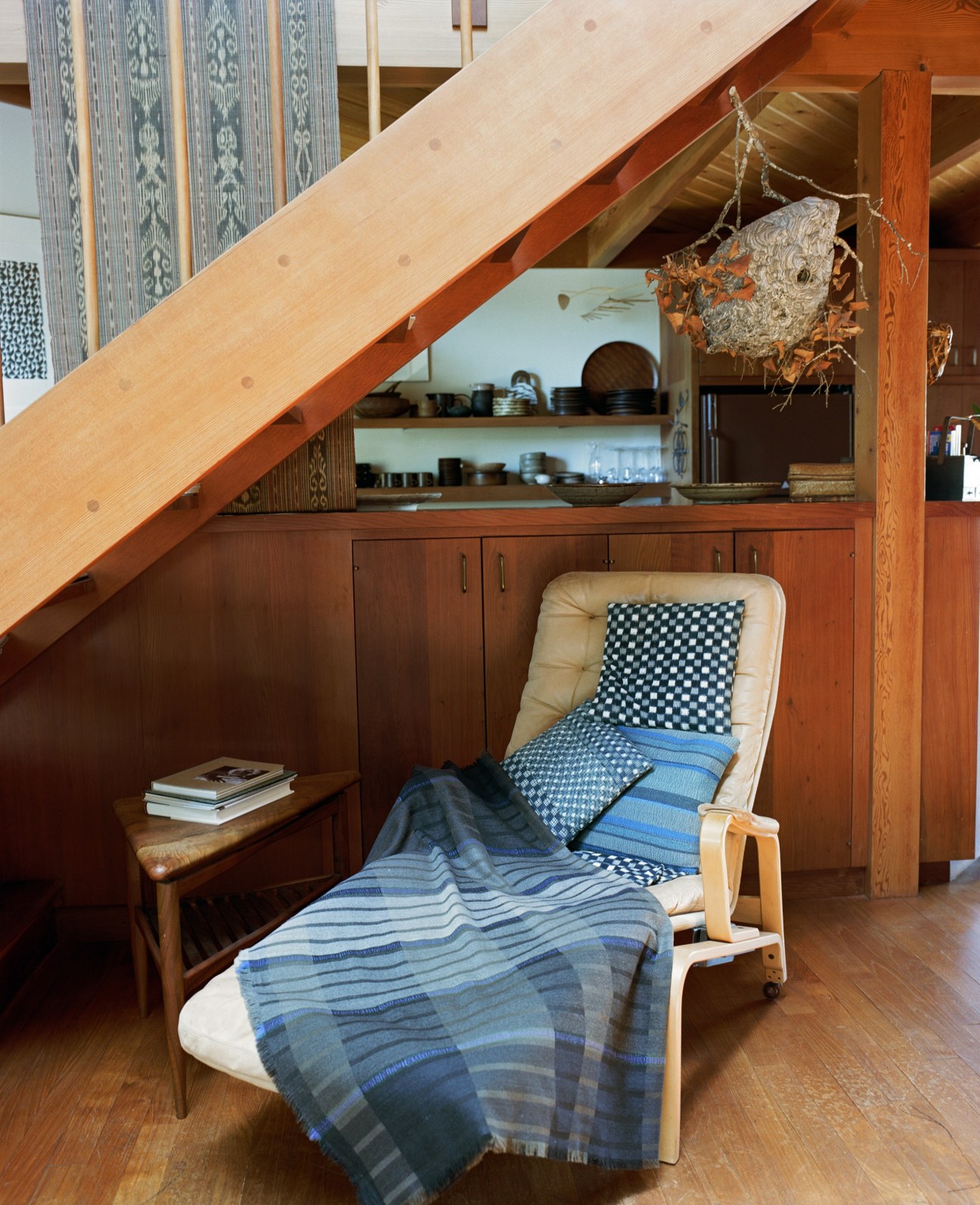 Wood-framed chair with woven textile blanket under angled ceiling beams and built-in storage.