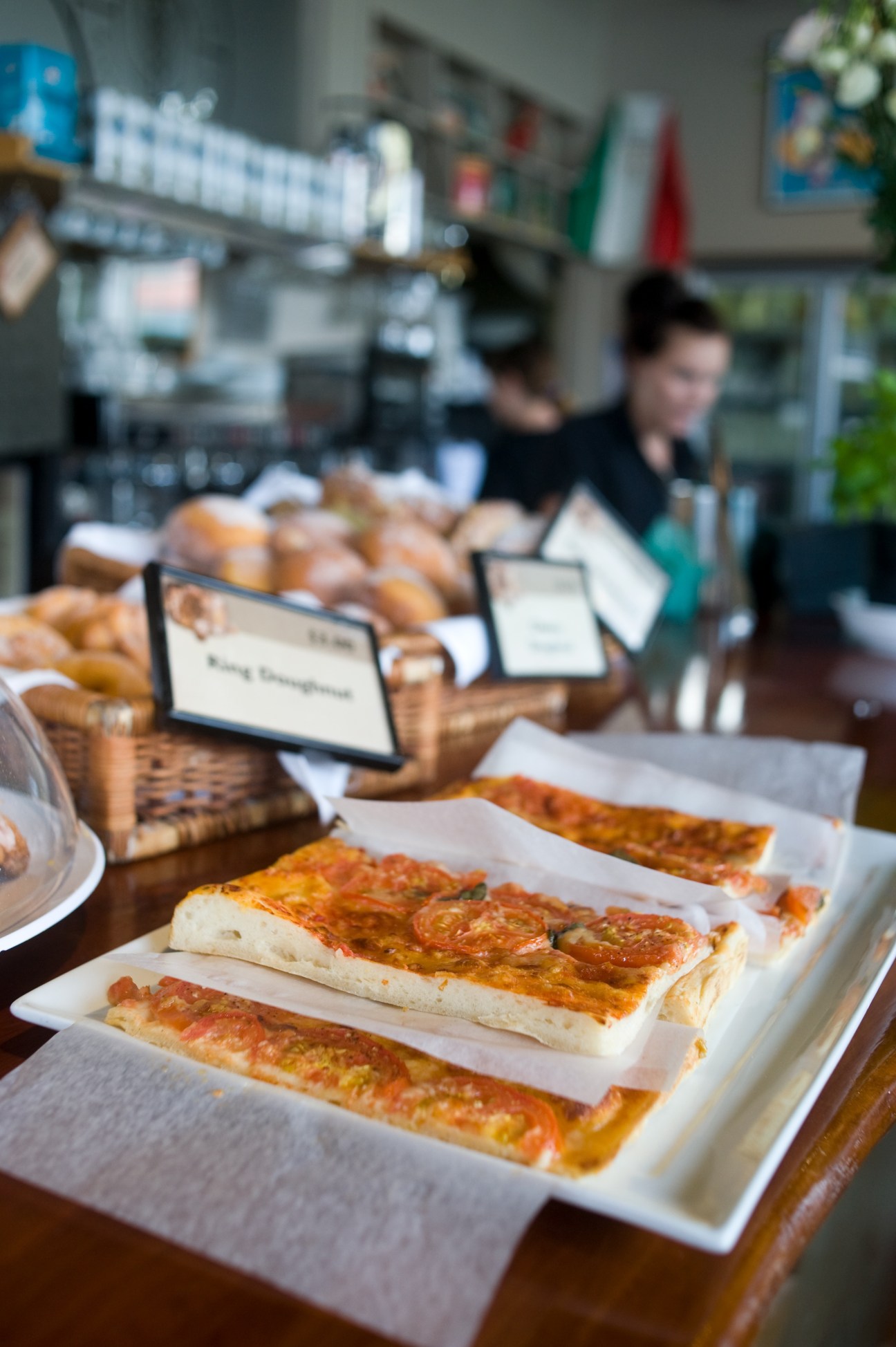 Sliced focaccia bread displayed on white plates at Il Forno bakery counter with staff in background.