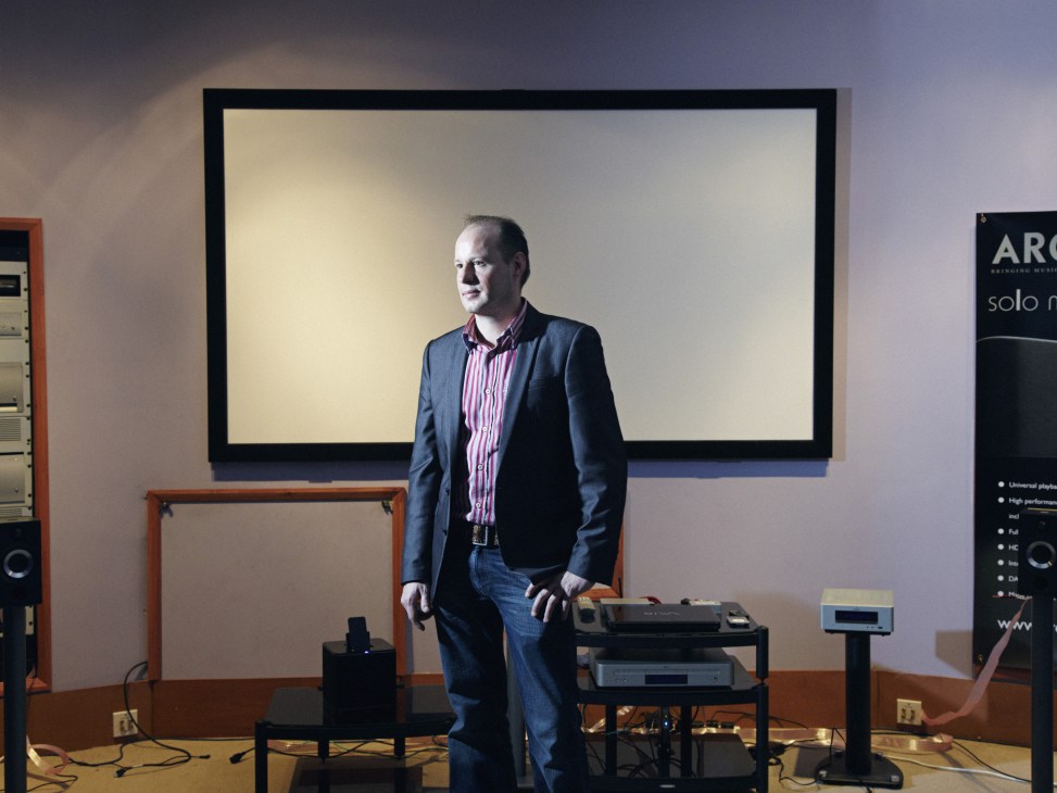 Senior engineer Andy Taylor standing in Arcam's showroom with audio equipment and display screen.