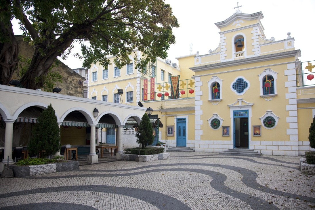 Colonial Portuguese square with yellow church, white arcaded building, and distinctive black-and-white patterned Calçada à Portuguesa stone paving.