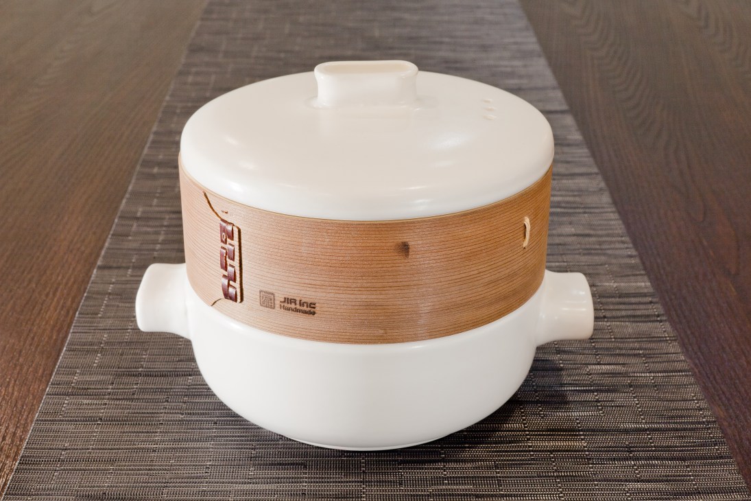 Jia Inc casserole pot with white ceramic body and natural wood band around the middle on a textured surface.