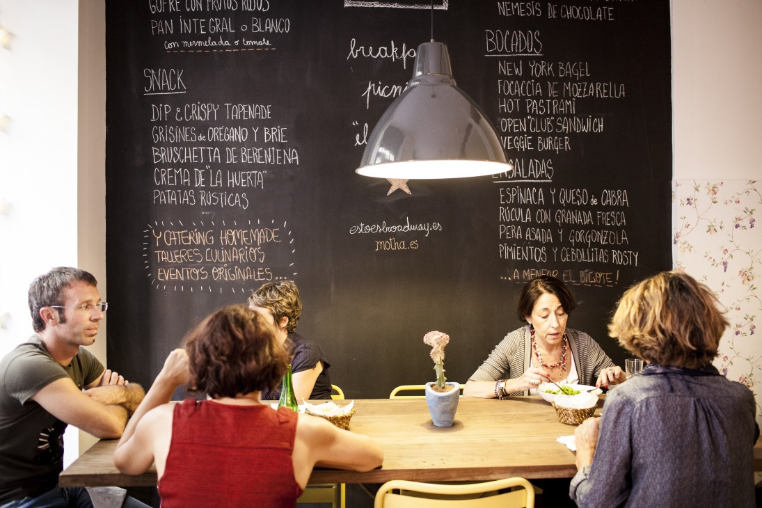 Diners enjoying lunch at wooden tables beneath a chalkboard menu at Motha café.