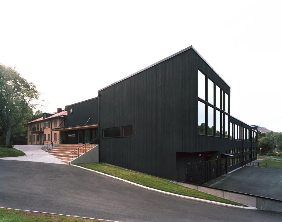 Modern black building with large windows adjacent to a renovated orange-brick house in Stockholm.