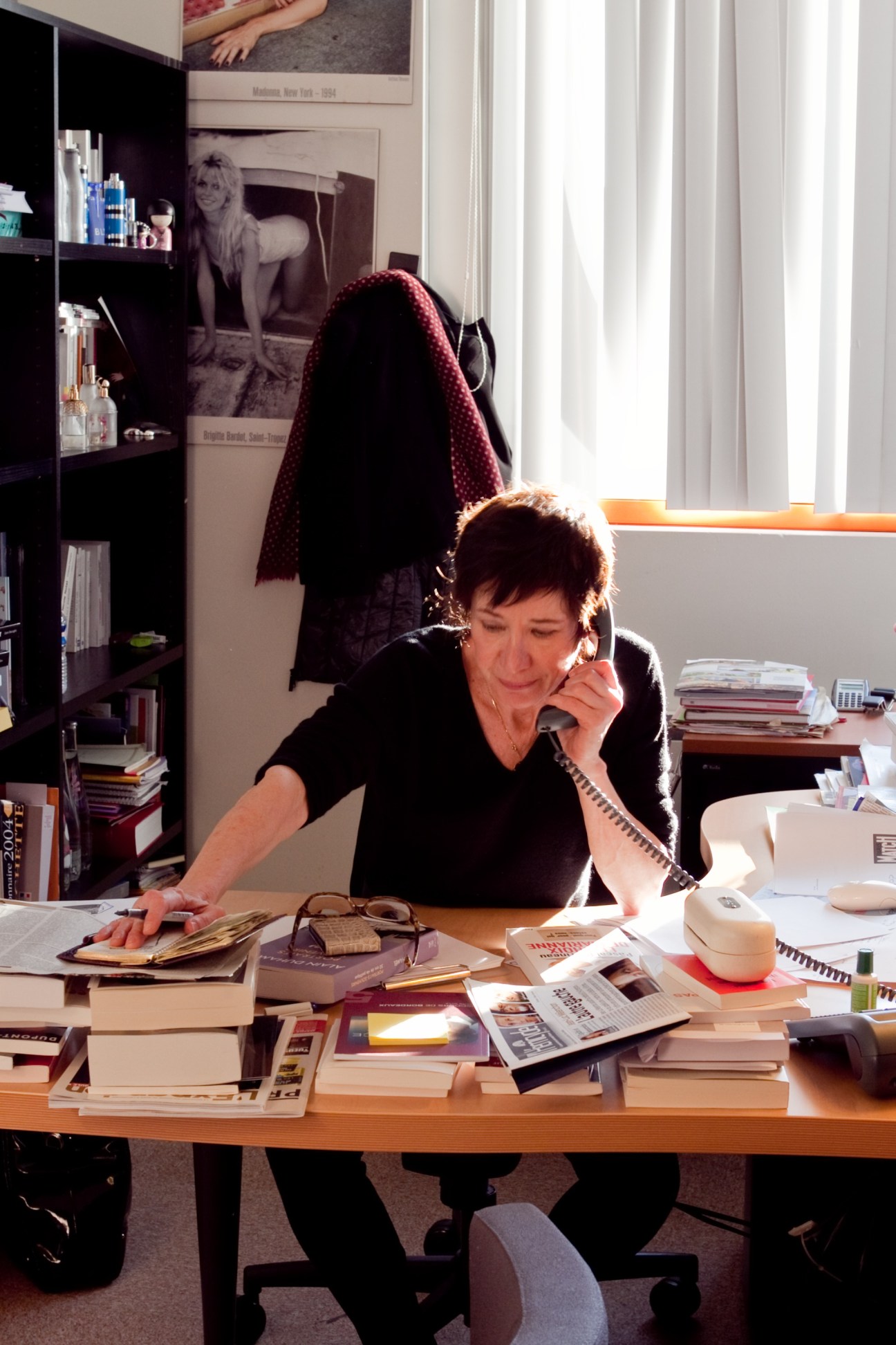 Editor Elisabeth Chavelet working at her desk with magazines and materials, speaking on a telephone.