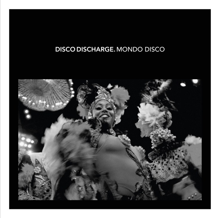 Black and white photograph of a disco performer in ornate sequined costume and headdress singing into a microphone.