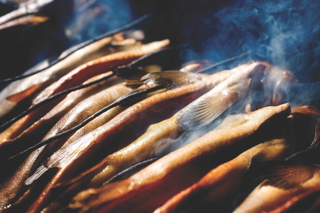 Smoked kippers lined up on a grill with smoke rising above them.