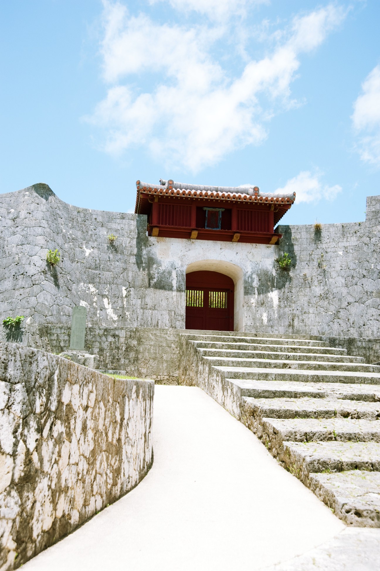 The rear gate of Shurijo castle with red roof structure and stone walls.