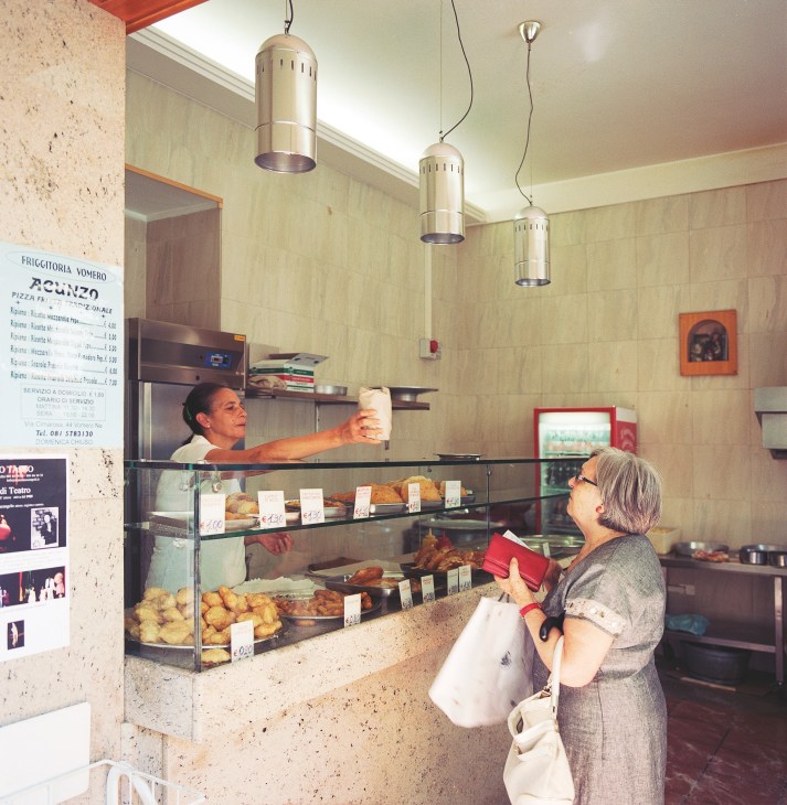 Customer ordering fried food at Friggitoria Vomero counter with display case of pastries.