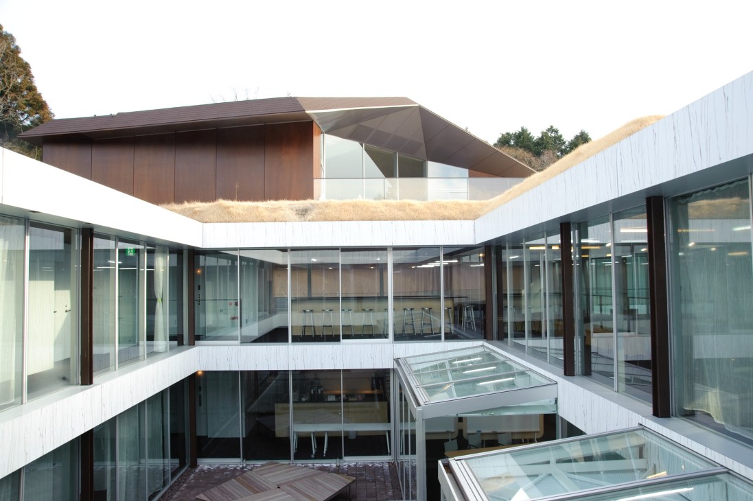 L-shaped building with angular roof and two interior courtyards surrounded by glass walls and forested landscape.