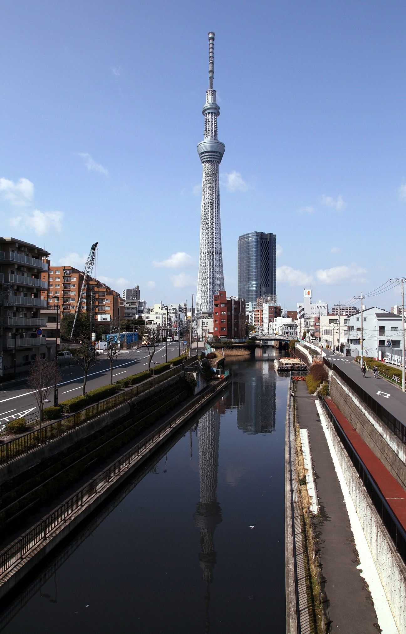Tokyo Sky Tree broadcasting tower reflected in a canal surrounded by urban buildings.